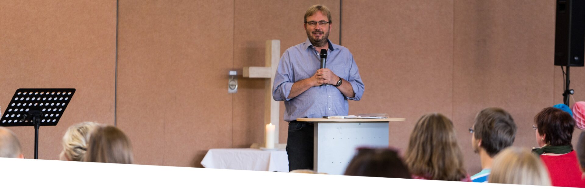 Ein Prediger begrüßt die Gemeinde von vorne.